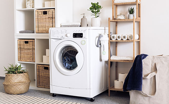 Image of white washing machine with bathroom towels next to it on the shelf.