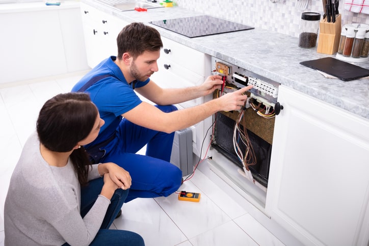 Image of a man repairing a broken dishwasher while the woman is focused on the appliance repair.