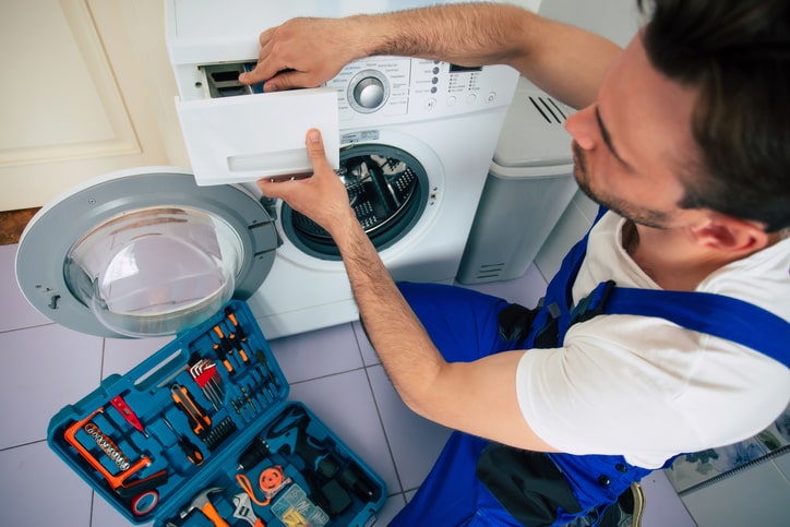 Image of a appliance repair technician man servicing/fixing a broken washing machine.